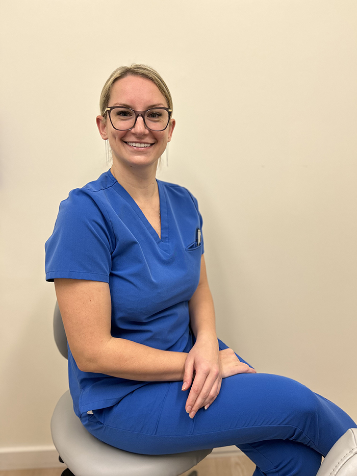 A female nurse sitting on a stool in front of a dental chair.