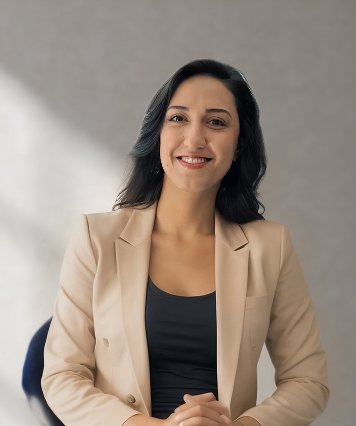 A woman sitting at a desk with a professional attire, smiling towards the camera.