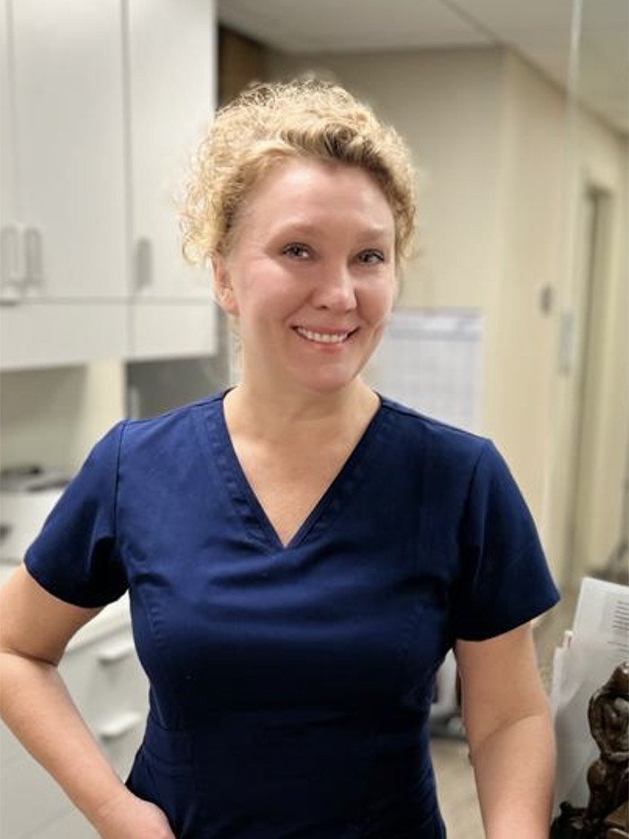 Woman wearing blue scrubs standing in front of mirror.