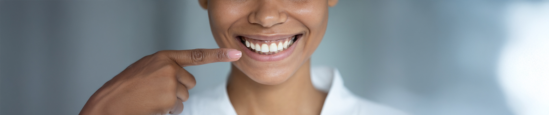 The image is a photograph of a woman with light skin, smiling at the camera. She appears to be in her late twenties or early thirties and has long hair. Her eyes are looking directly at the camera, and she is holding up her index finger near her mouth as if she s making a point or emphasizing something. The background is plain and light-colored, which suggests that this could be a stock photo used for various purposes such as advertising, personal branding, or lifestyle content.