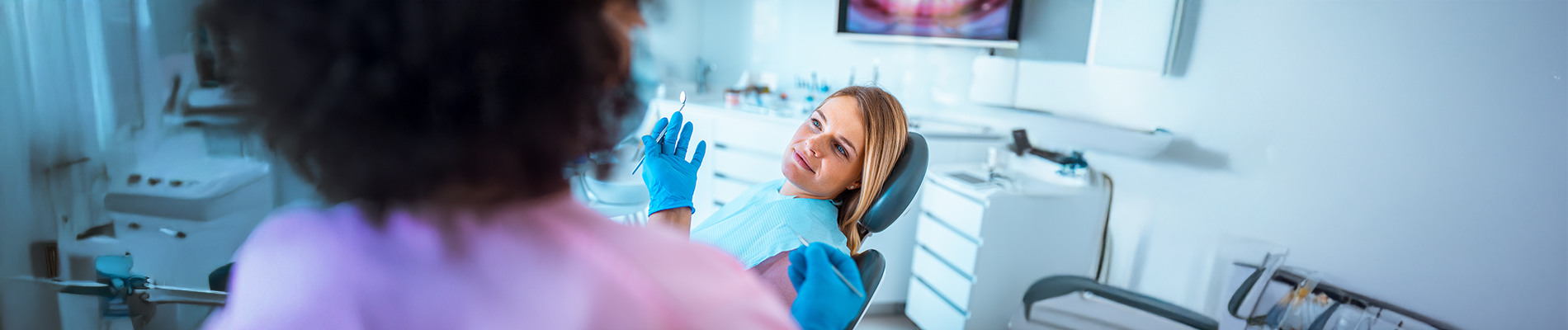 An image depicting a dental clinic scene with two people  one seated in a dentist s chair, receiving oral care from another person who appears to be a dental professional.