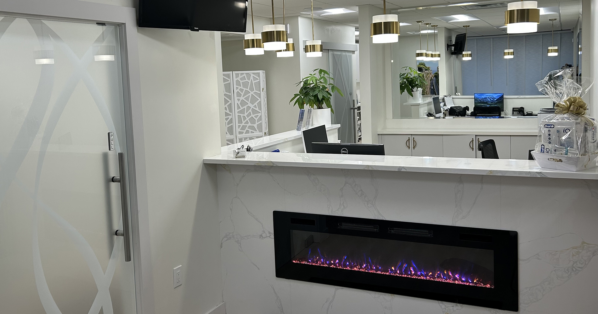 This is an interior view of a modern office space with a reception area featuring a fireplace, a counter with a sink, and a large window.