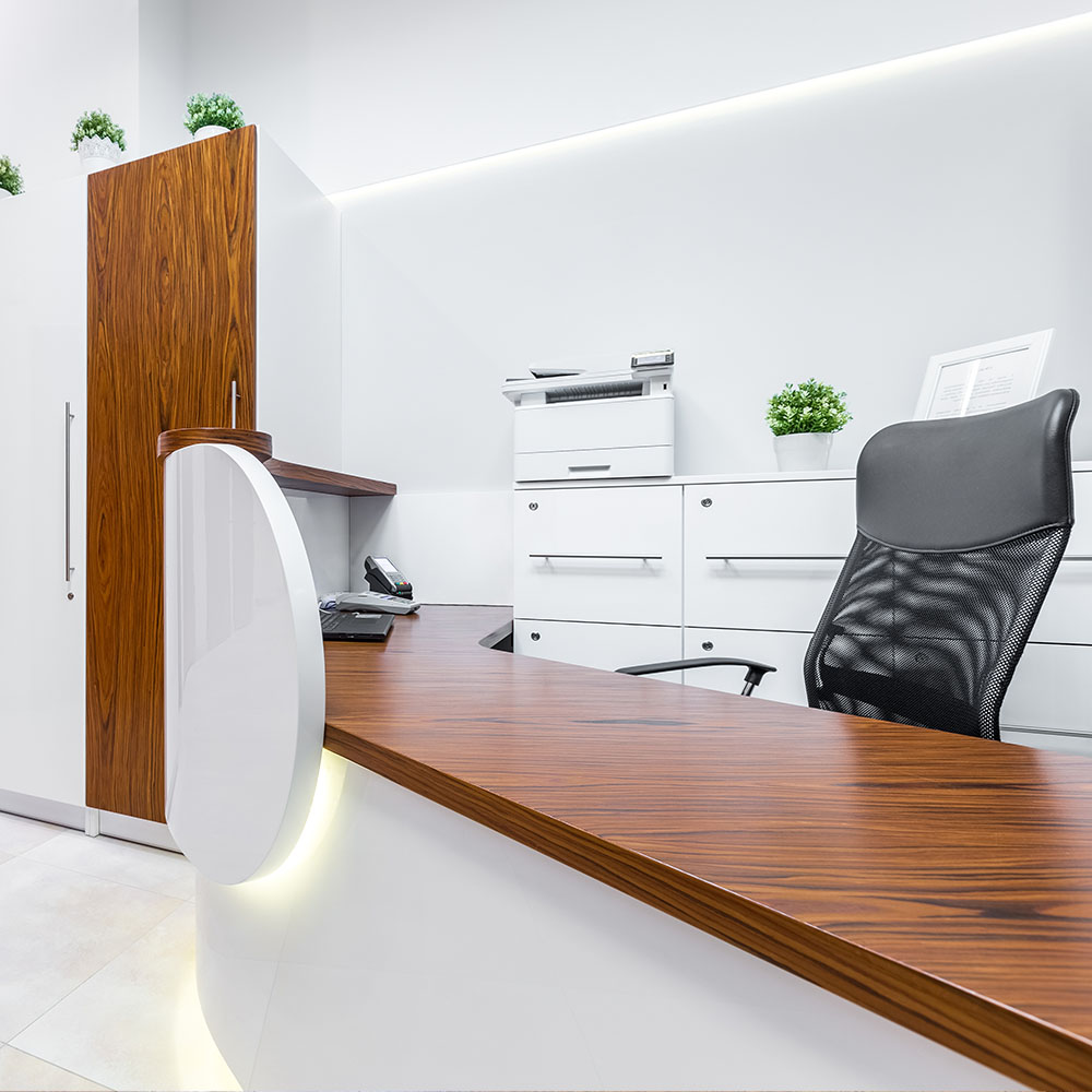 The image shows a modern office space with a sleek desk, chair, and computer setup, featuring wood paneling, a white countertop, and a contemporary design.