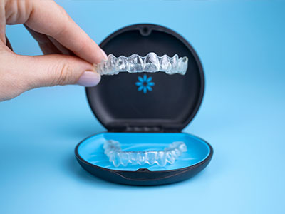 An image featuring a hand holding an open, transparent case containing a set of clear dental aligners against a blue background.